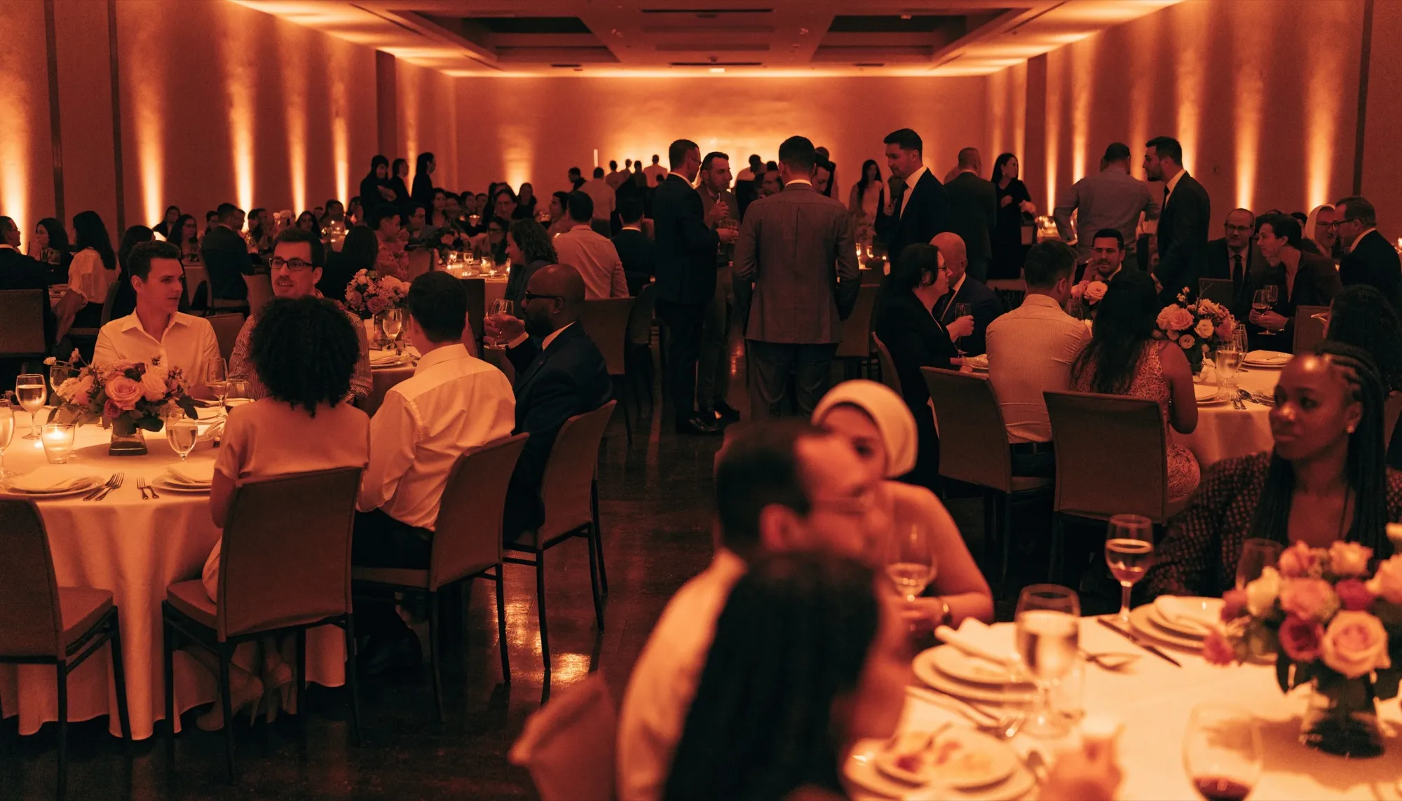 A corporate gala dinner in a hotel ballroom, with round tables under warm amber lighting and guests talking
