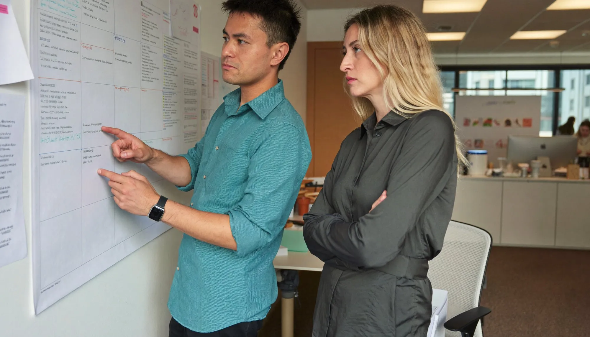 A wall planner in a Dubai office marked up in coloured pen, with two colleagues standing in front of it mid-discussion